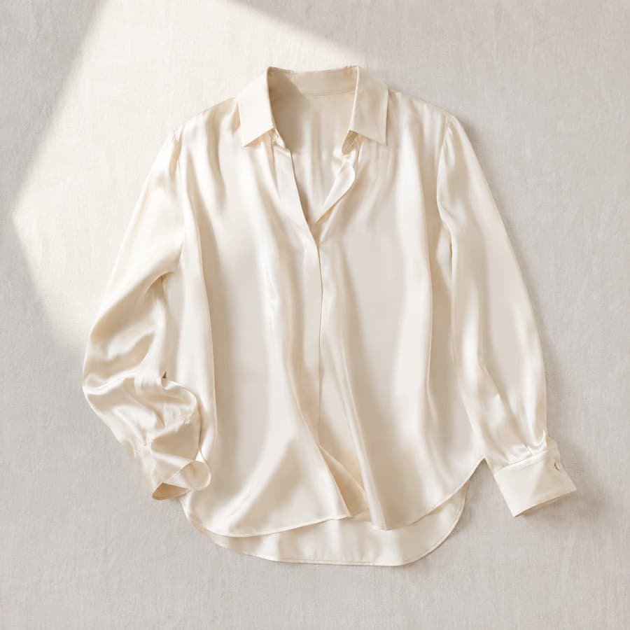 Blusa de seda color crema fotografiada en plano cenital sobre lino claro
